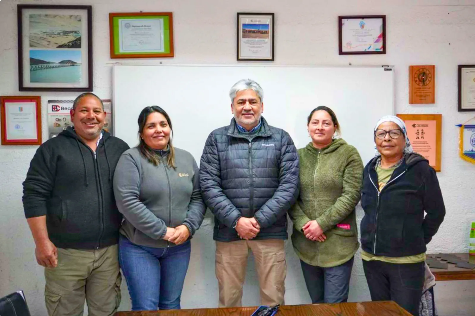 Cinco personas posan en una oficina con diplomas