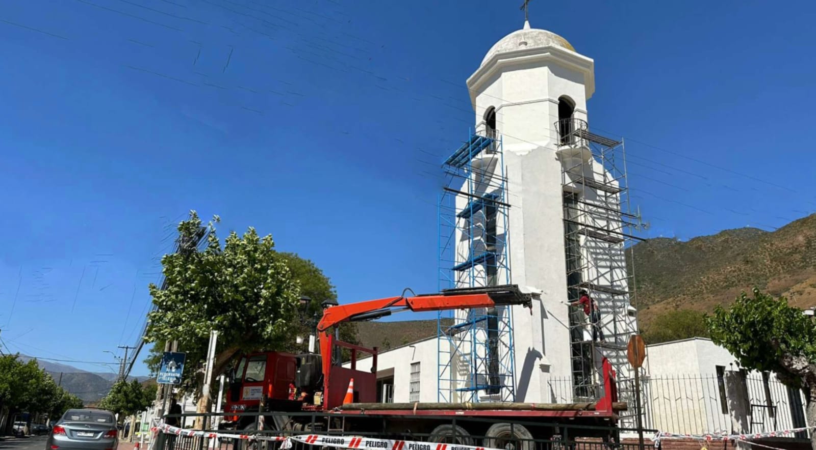 Campanario blanco en restauración con andamios y grúa