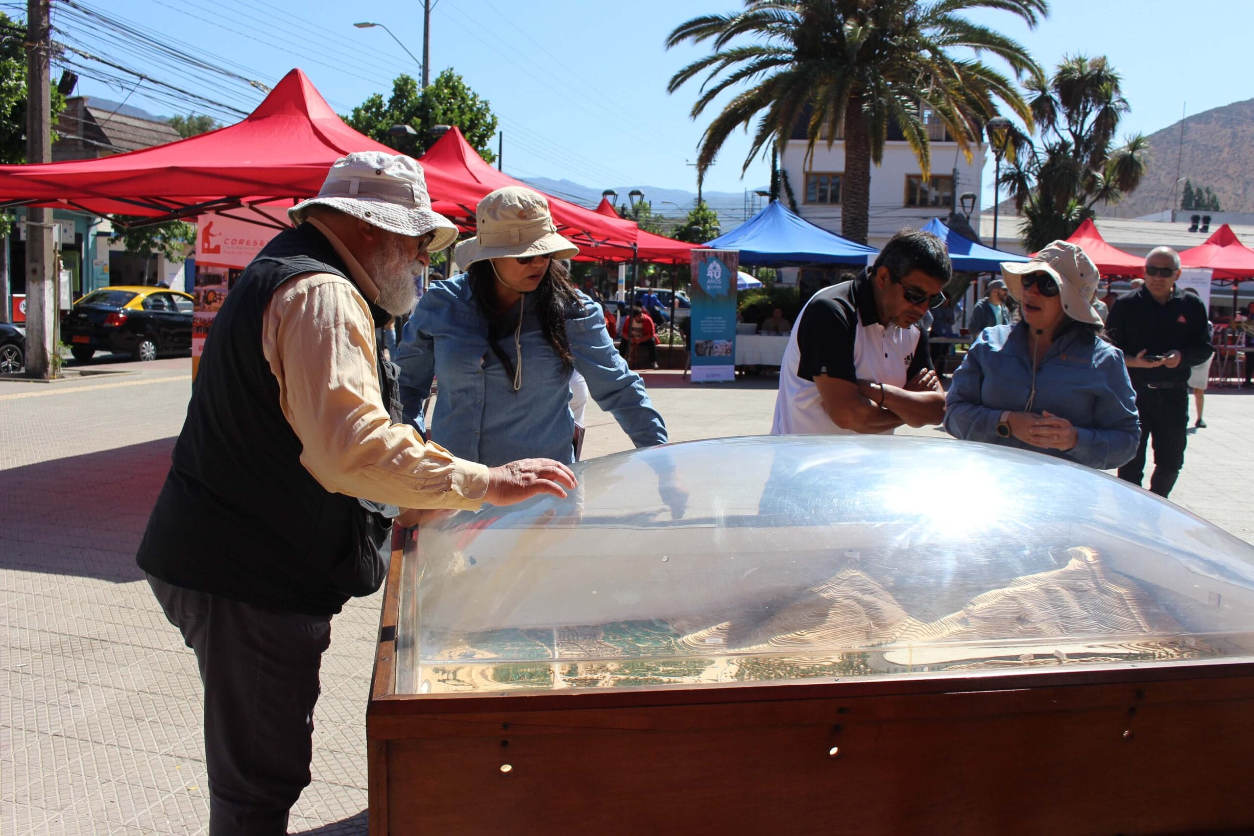 Personas observando maqueta urbana en plaza soleada