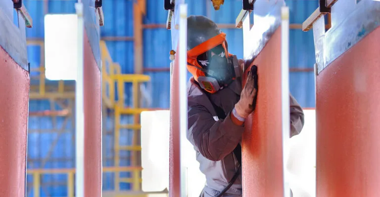 Trabajador industrial lijando vigas metálicas con protección