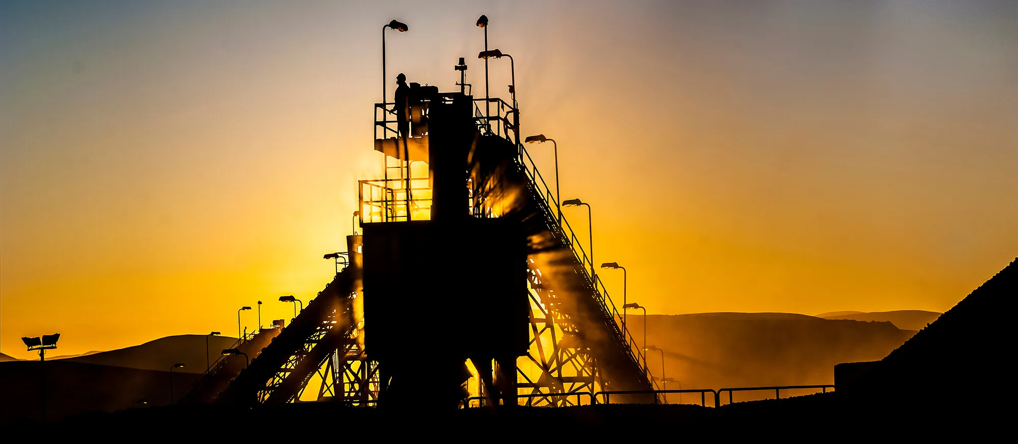 Planta industrial al atardecer con silueta de trabajador