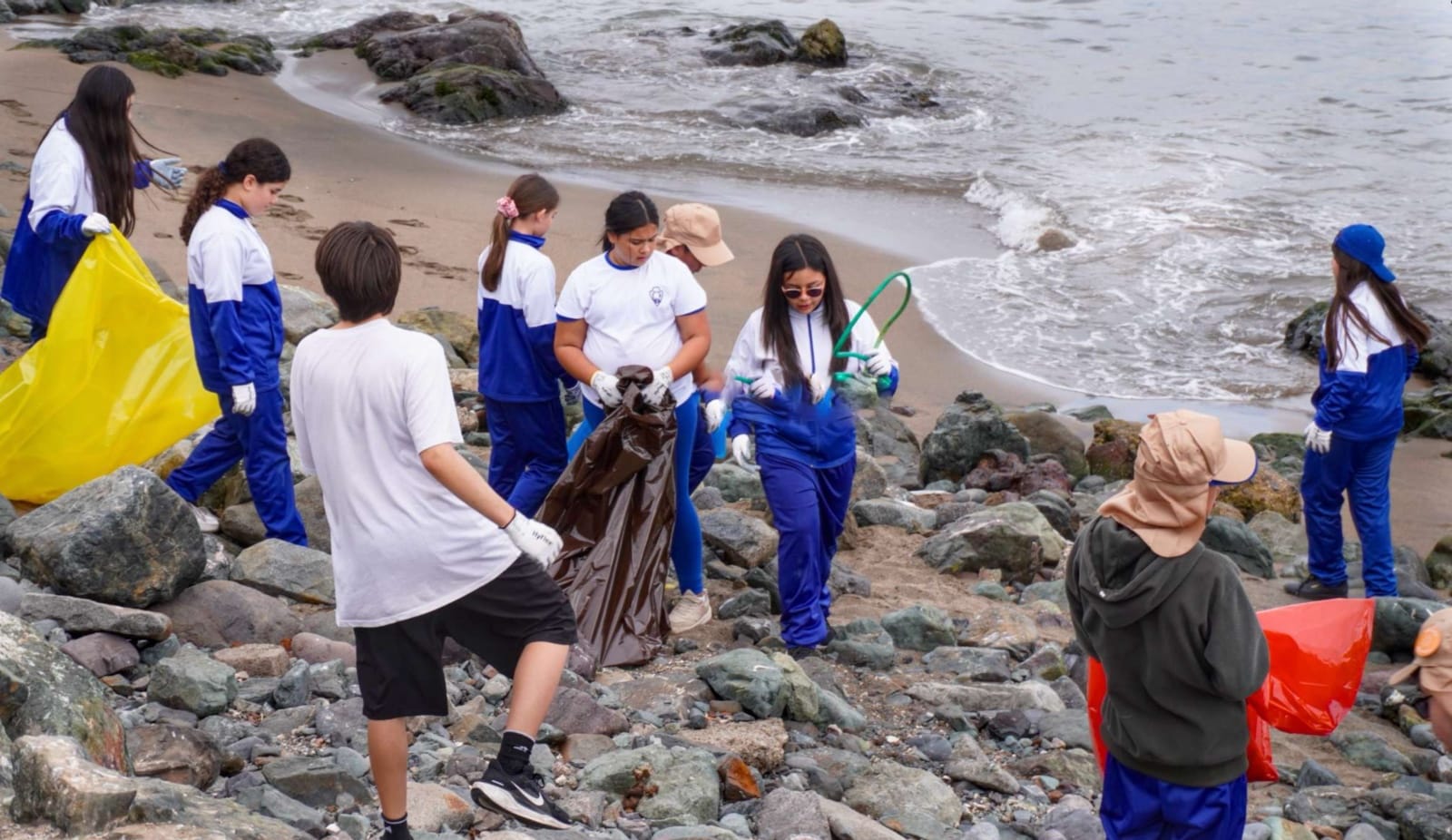 Estudiantes recogiendo basura en playa rocosa