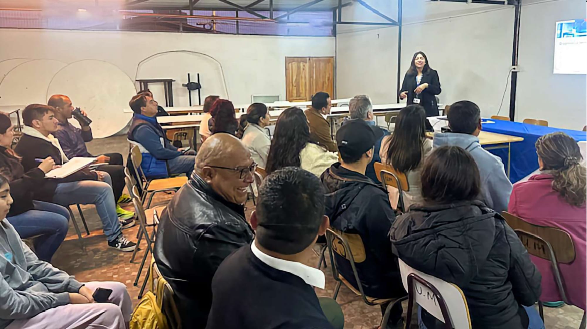 Mujer dando charla ante público en aula